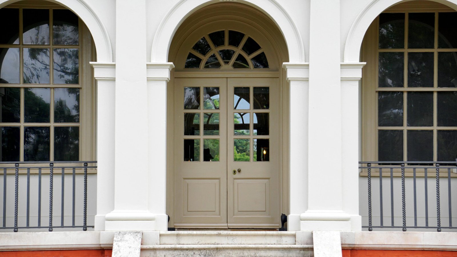 Front view of a classic white building entrance with arched doorway and columns, featuring glass windows and metal railings.