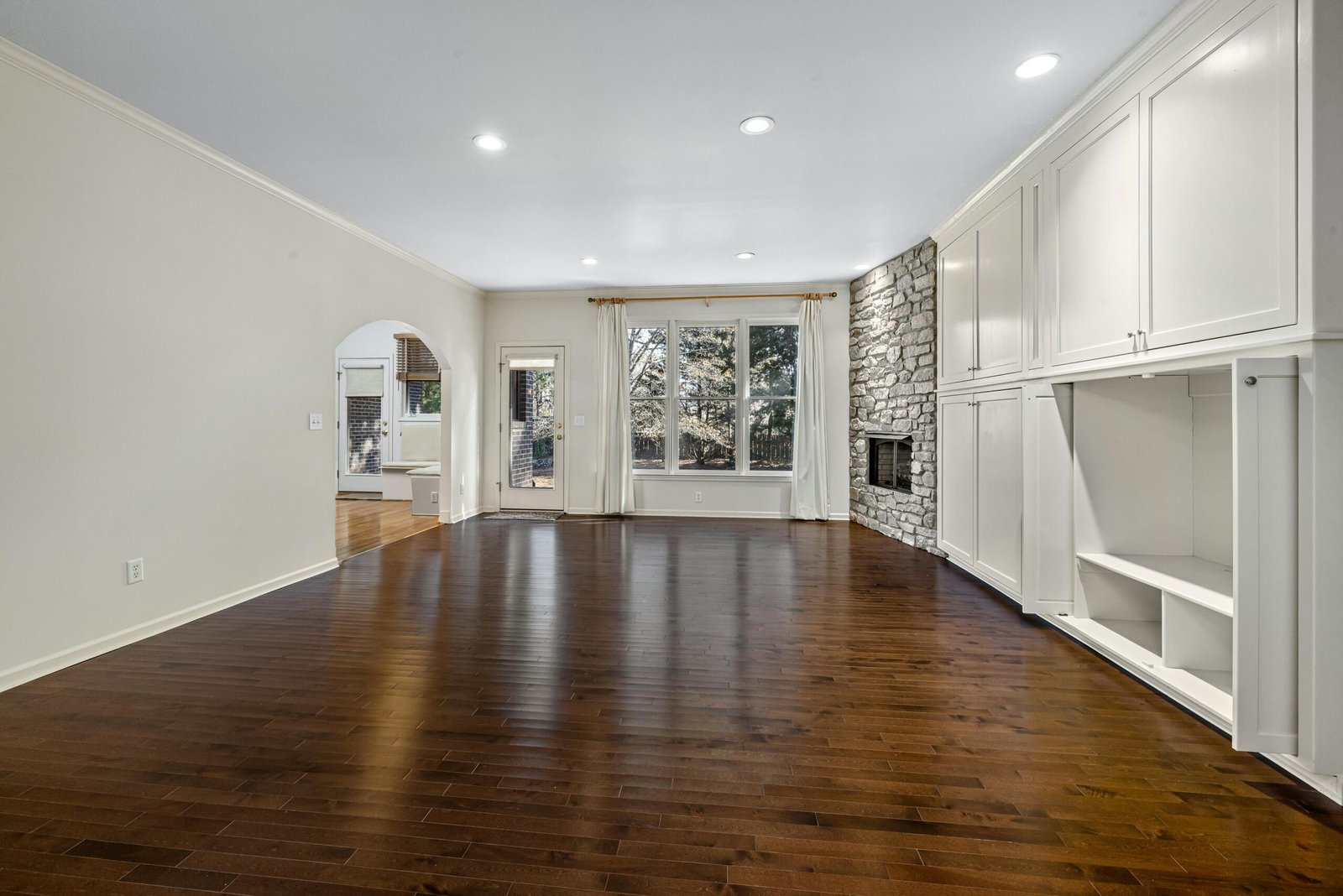 Bright, empty living room featuring hardwood floors and stone fireplace.